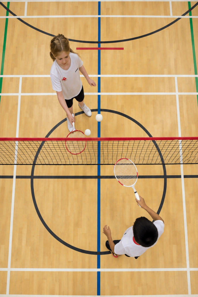 Children practicing badminton across an indoor net