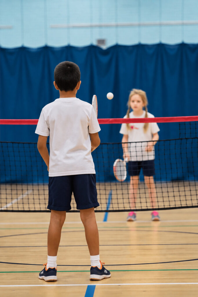 Children playing badminton on an indoor court